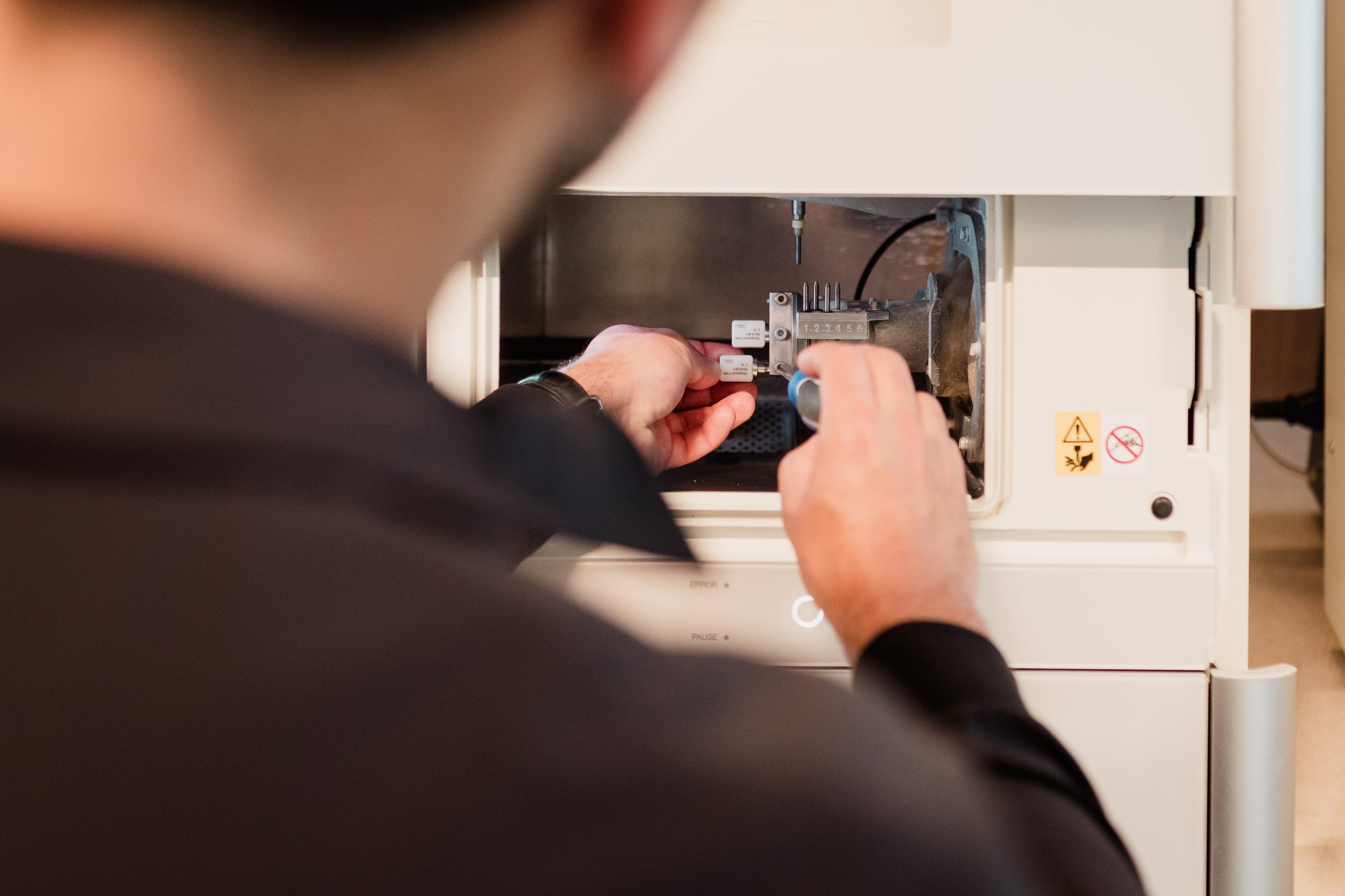 Manos cargando bloques de cerámica CAD en la fresadora del laboratorio